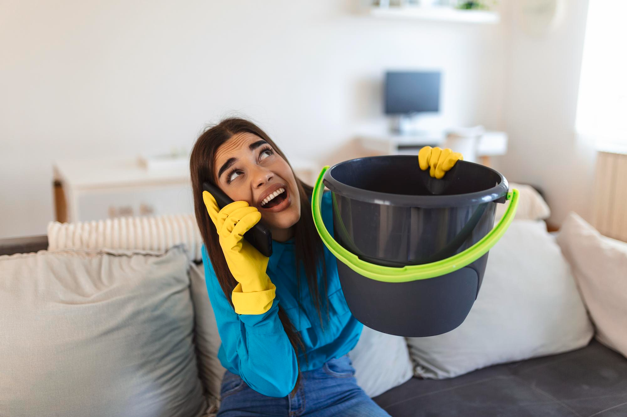 A woman in distress tries to collect water from a leaking ceiling into a bucket